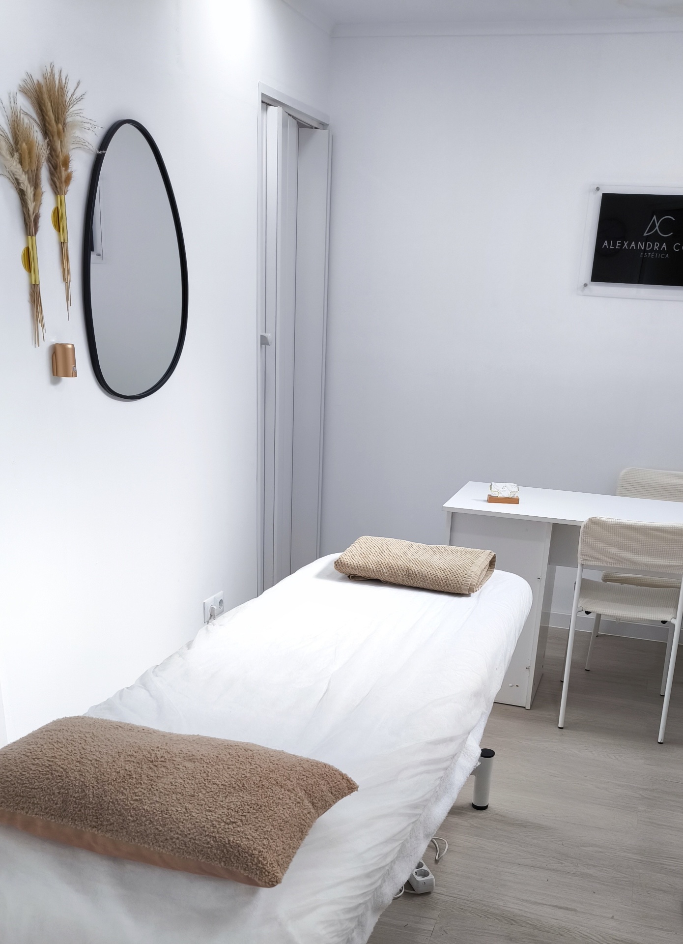 Sala de tratamento da Alexandra Costa Estética com marquesa, espelho oval e identidade visual da clínica